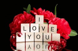 I Love You wooden tiles on a mirror with joy word reflection and red carnations and ribbon isolated on black