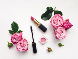 Decorative flat lay composition with mascara, lipstick and blush, decorated with flowers. Top view on white background, view from above