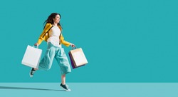 Cheerful happy woman enjoying shopping: she is carrying shopping bags and running to get the latest offers at the shopping center