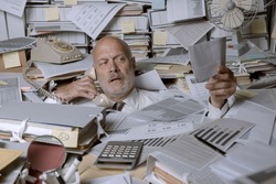 Stressed businessman overwhelmed by work, he is drowning under a lot of paperwork and answering phone calls