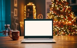 Laptop with blank screen on a desktop and Christmas tree with lights in the background