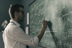 Young smart mathematician drawing math formulas on the chalkboard and thinking: he is solving problems and discovering new theories