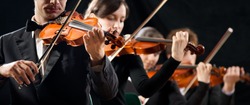 Violin orchestra performing on stage on dark background.