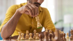 Man playing chess at home, he is moving a piece on the chessboard, strategy games concept