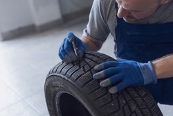 Mechanic checking tire tread depth and wear using a tire gauge, car maintenance concept