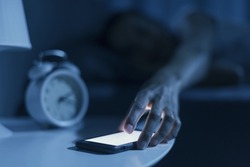 Woman sleeping in her bed and receiving a phone call late at night, she is checking her smartphone