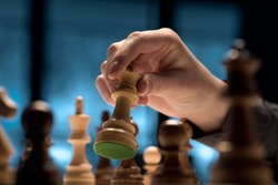 Man playing chess and moving a piece on the chessboard, hand close up, strategy games concept