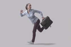 Scared businesswoman escaping from danger, she is running away and looking backwards, isolated on gray background