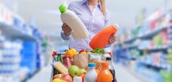 Woman doing grocery shopping at the supermarket and comparing products, she is checking two bottles of laundry detergent