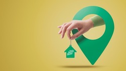 Hand holding house shaped keychain and location pin, real estate concept