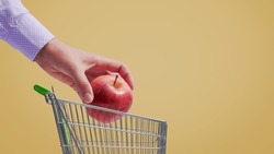 Customer putting an apple in a small shopping cart, grocery shopping concept