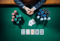 Poker player's hands with cards and stacks of chips all around on green table, top view