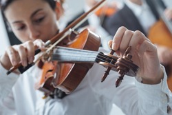 Woman tuning her violing and rotating pegs, cello player on background, selective focus