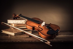 Violin, bow and old books on a rustic wooden table, arts and music concept