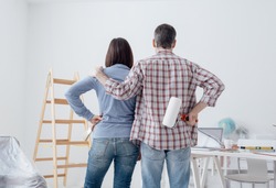 Loving couple staring at their freshly painted room, back view: home renovation and relationships concept