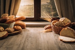Fresh bread on the kitchen table in front of a window with a countryside panorama, healthy eating and traditional bakery concept