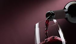 Pouring red wine from a bottle into a wineglass: wine tasting and celebration