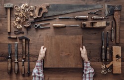 Carpenter holding a wood block and collection of vintage woodworking tools on a workbench, craftsmanship and handwork concept
