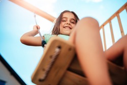 Low angle view of a little girl wearing green shirt sitting on the swing at backyard playground