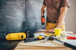 Man drilling wood with battery power Drill on the table at home
