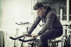 Attractive young man exercising in gym: spinning, exercizing on stationary bike
