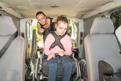A disabled child in a wheelchair being helped into a specially adapted van / Working with disability