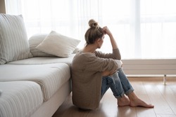 A depressed woman is sitting on the floor in the living room.