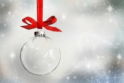 Transparent Christmas ball hanging on red ribbon on snowy winter background