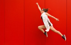 Stylish woman dancing and jumping on a street against a red wall