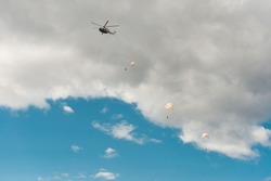 Paratroopers with parachutes are going down landing, left helicopter