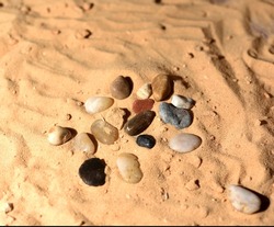 stones on a sandy beach in the shape of a handmade symbol, golden sand background.