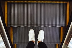 Selfie of  man feet in white sneaker shoes on escalator steps in the shopping mall, top view in vintage style