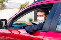 Young male driver inside car with protective face mask
