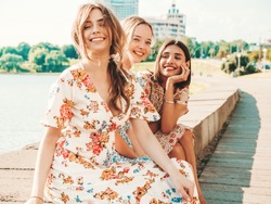 Three young beautiful smiling hipster girls in trendy summer sundress.Sexy carefree women posing on the street background. Positive models having fun and hugging. Sitting after shopping