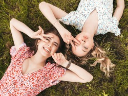 Two young beautiful smiling hipster girls in trendy summer sundress.Sexy carefree women lying on the green grass in sunglasses.Positive models having fun.Top view.They show peace sign