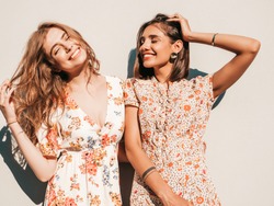 Two young beautiful smiling hipster girls in trendy summer sundress.Sexy carefree women posing near wall on the street background. Positive models having fun and hugging