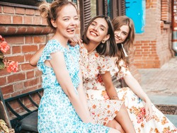 Three young beautiful smiling hipster girls in trendy summer sundress.Sexy carefree women posing on the street background.Models having fun and hugging. Sitting on the bench after shopping
