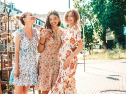 Three young beautiful smiling hipster girls in trendy summer sundress.Sexy carefree women posing on the street background.Models having fun and hugging.Discussing and walking after shopping