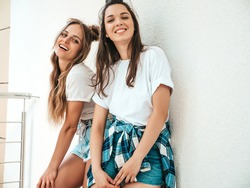 Portrait of two young beautiful smiling hipster female in trendy summer white t-shirt clothes.Sexy carefree women posing in street near white wall. Positive models having fun, hugging and going crazy