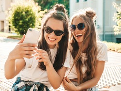 Portrait of two young beautiful smiling hipster women in trendy summer white t-shirt clothes.Sexy carefree women posing on street background. Positive models having fun, hugging and taking selfie