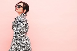 High fashion portrait of young beautiful brunette woman wearing nice trendy summer zebra coat.Sexy fashion model posing near pink wall in studio.Fashionable female in sunglasses