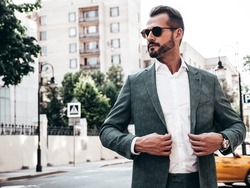Portrait of handsome confident stylish hipster lambersexual model.Sexy modern man dressed in elegant suit. Fashion male posing in the street background in Europe city at sunset. In sunglasses