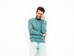 Handsome smiling hipster  model.Sexy unshaven man dressed in summer stylish blue sweater and jeans clothes. Fashion male with curly hairstyle posing in studio. Isolated on white