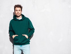 Handsome confident hipster  model.Sexy unshaven man dressed in summer stylish green hoodie and jeans clothes. Fashion male with curly hairstyle posing in studio. Isolated on grey