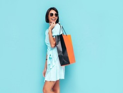 Portrait of young beautiful smiling female in trendy summer dress. Carefree woman posing near blue wall in studio. Positive model holding shopping bag. Cheerful and happy. Isolated