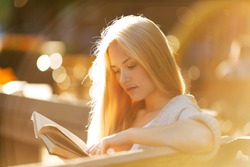 Happy blonde girl sitting and reading a book