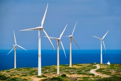 Green renewable alternative energy concept - wind generator turbines generating electricity. Wind farm on Crete island, Greece with small white church