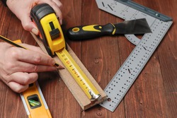 horizontal view from above of two hands using a pencil and a flexometer to measure the lenght of a wood strip on a set with others DIY tools