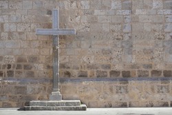 horizontal view of a large stone cross, symbol of catholic church, in front of a church wall