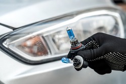 The mechanic's hands hold halogen car bulbs against headlight, repair auto